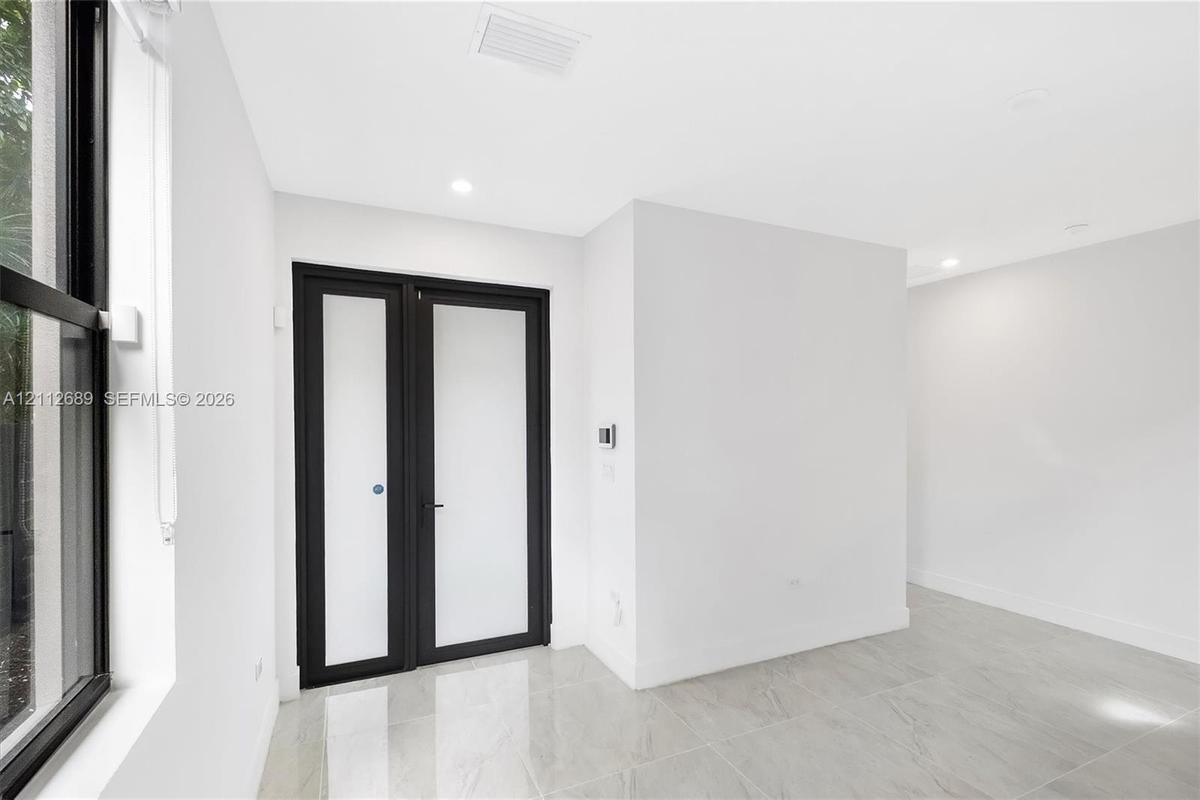 Neutral-toned tile flooring, recessed ceiling lighting, and double doors featuring frosted glass panels with matte black frames