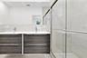 Floating wood-finish double vanity with dual undermount sinks and chrome fixtures, large wall-mounted mirror, and walk-in shower featuring glass slidi