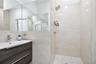 Modern floating vanity with a dark wood-finish exterior, integrated rectangular sink, wall-spanning mirror, and a walk-in shower featuring large-forma