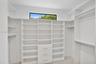 Walk-in closet featuring floor-to-ceiling white built-in shelving, integrated dresser drawers with metallic pulls, horizontal hanging rods, and a cler