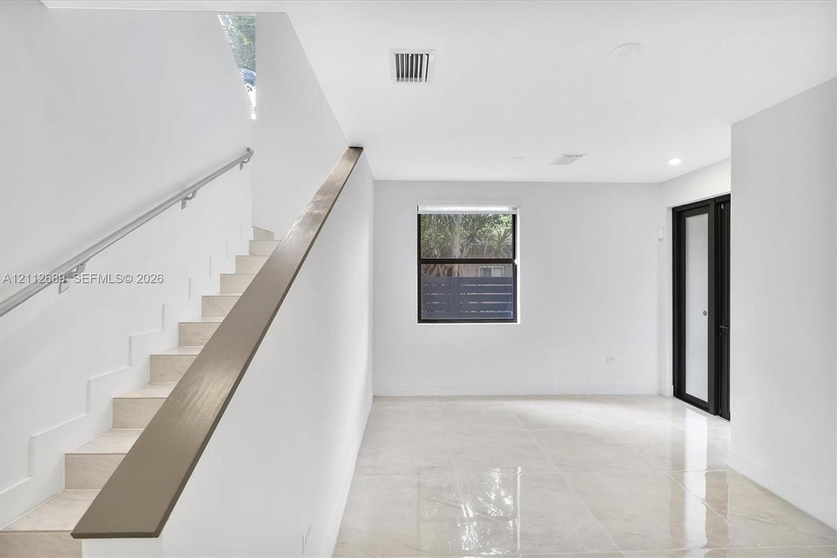 Interior space featuring polished tile flooring, a staircase with a minimalist metal handrail, a dark-finished accent banister, and a door with black 