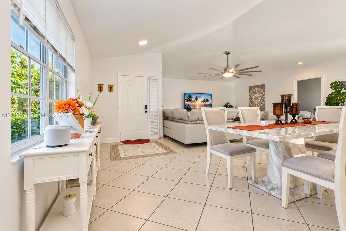Open-concept area featuring vaulted ceilings, oversized grid-pattern windows, large-format tile flooring, and a multi-blade modern ceiling fan
