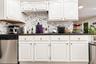 White raised-panel cabinetry, dark stone-finish countertops, high-contrast patterned backsplash, and stainless steel dishwasher