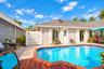 Outdoor living area featuring a custom-shaped swimming pool with brick coping, wood-finish decking, and light-colored horizontal siding