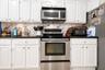 Kitchen featuring white raised-panel cabinetry, dark solid-surface countertops, patterned tile backsplash, and stainless steel appliances including an