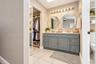 Bathroom vanity featuring a slate-toned cabinetry base, dual circular wall mirrors, a multi-bulb vanity light fixture, light-toned countertop, and sli