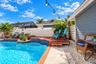 In-ground swimming pool with patterned tile border, raised wood decking, horizontal slat fencing, and stone landscape ground cover