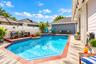 Outdoor swimming pool featuring decorative tile accents, a brick paver border, concrete patio, and white horizontal privacy fencing