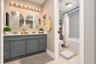 Dual-sink vanity with gray cabinetry and solid-surface countertop, circular wall mirrors, multi-bulb vanity lighting, and recessed wall shelving