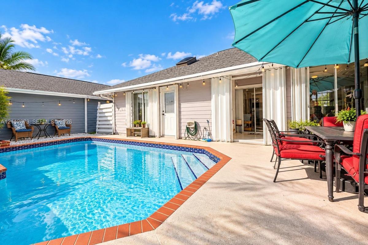 Outdoor living area featuring a swimming pool with tile trim, concrete patio surfacing, horizontal lap siding, and attached string lighting