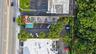 Aerial perspective of property featuring paved surface parking, mature perimeter trees, and street-front access