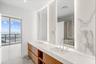 Dual-sink vanity with wood-finish cabinetry, stone-surface countertop, floor-to-ceiling stone-tiled backsplash with integrated vertical lighting, and 