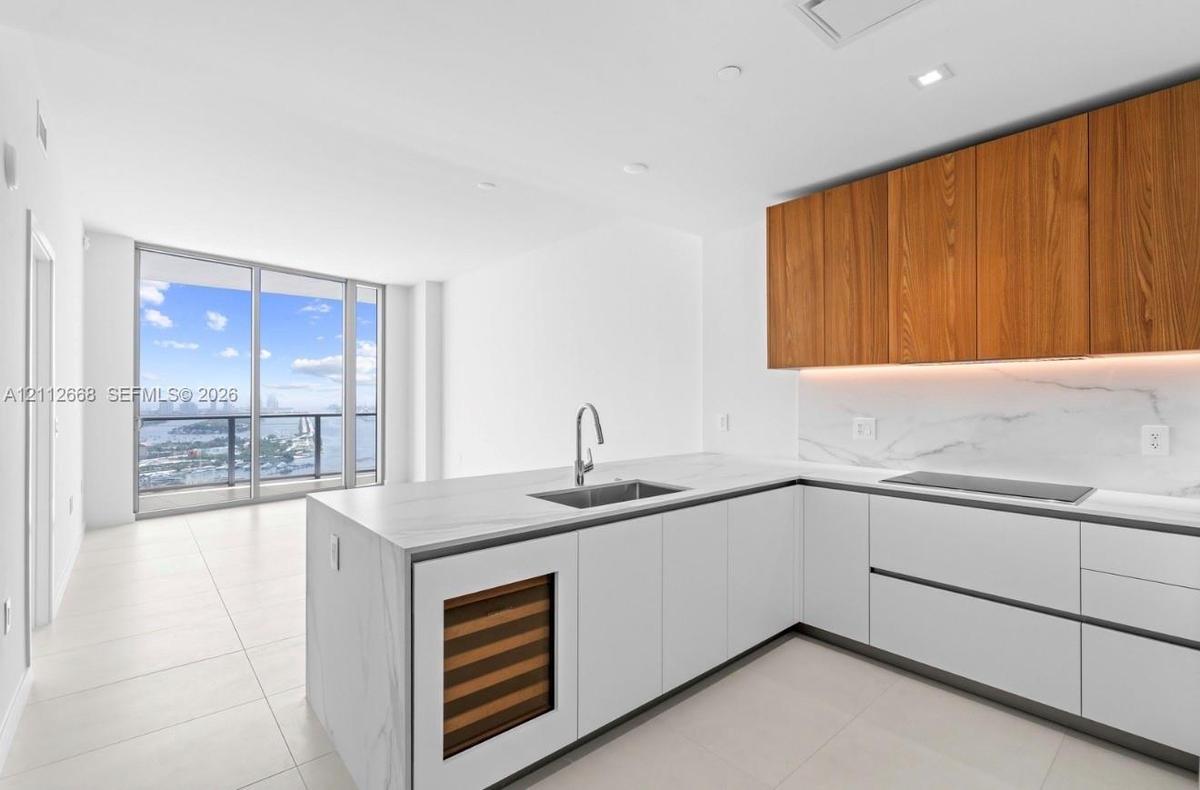 Kitchen featuring white flat-panel cabinetry, wood-finish upper cabinets, stone-surfaced countertops, a built-in wine cooler, and floor-to-ceiling win