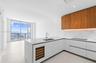 Kitchen featuring white flat-panel cabinetry, wood-finish upper cabinets, stone-surfaced countertops, a built-in wine cooler, and floor-to-ceiling win