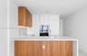 Modern kitchen featuring custom wood-finish cabinetry, white flat-panel cabinetry, waterfall-edge stone countertops, integrated appliances, and a stai