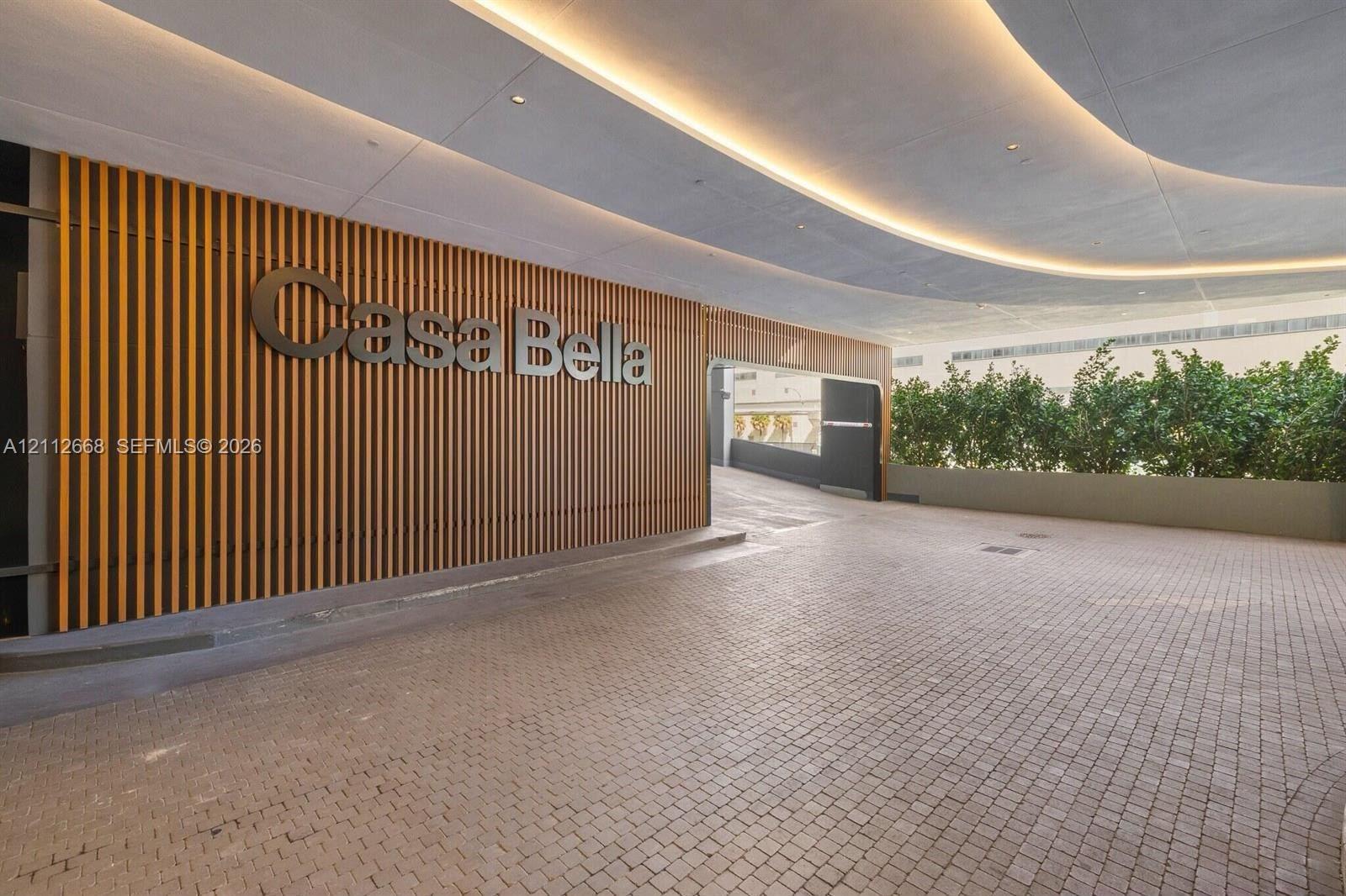 Covered arrival entrance featuring a stone paver driveway, vertical wood-slat wall accents, recessed architectural lighting, and integrated landscapin