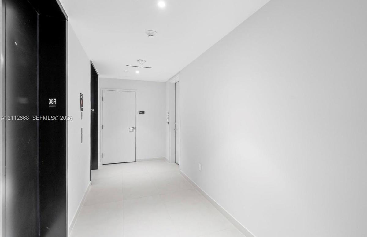 Minimalist hallway featuring white tile flooring, high-contrast black elevator doors, and recessed ceiling lighting