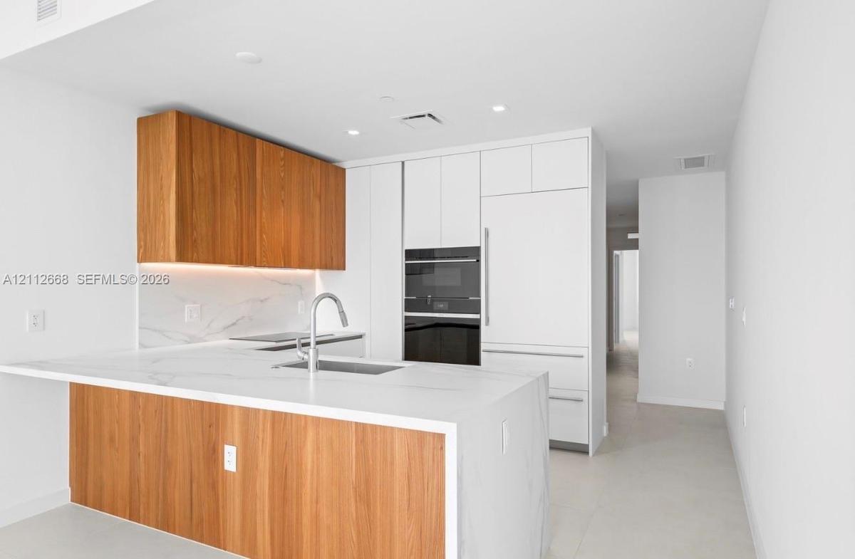 Kitchen featuring flat-panel wood-finish cabinetry, white solid surface countertops with integrated backsplash, built-in panel-ready refrigerator, sta