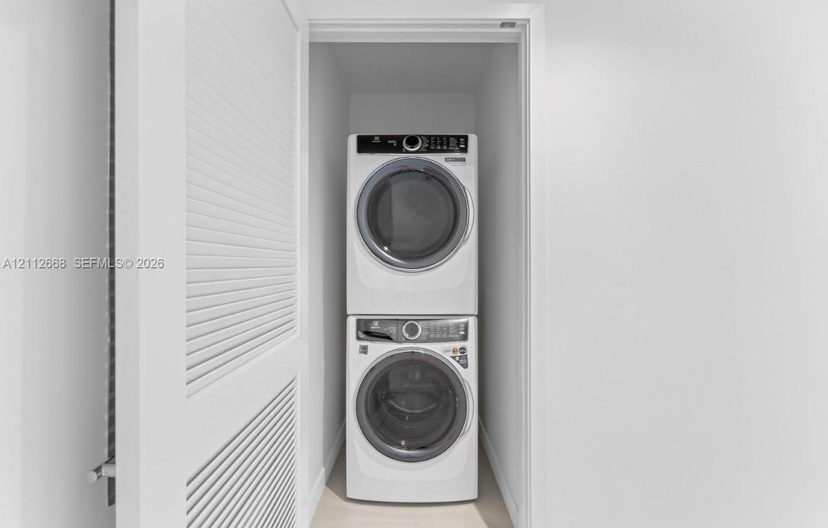 Laundry closet featuring a stacked washer and dryer set, neutral wall finish, and white louvered door