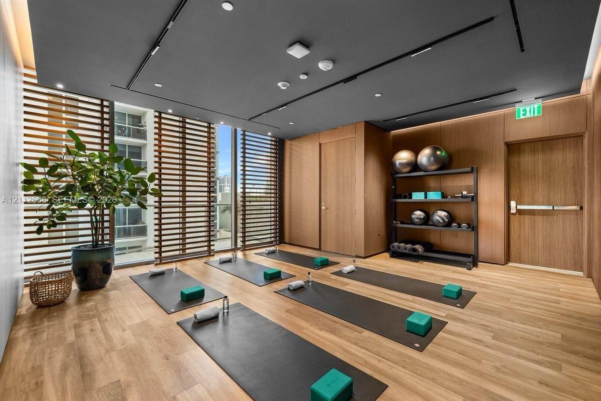 Fitness room featuring wood-finish flooring, wood-paneled walls, floor-to-ceiling slatted privacy screens, and a recessed ceiling with integrated line