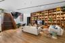 Expansive room featuring wood-finish flooring, floor-to-ceiling built-in wooden shelving, a floating-style staircase with wood treads, and recessed tr