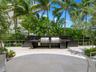 Outdoor kitchen featuring a dark stone-finish backsplash and countertop, stainless steel dual grills, integrated refrigeration, and a stone-tiled pati