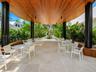 Covered outdoor patio featuring a vaulted wood-slat ceiling, structural cylindrical pillars, built-in wooden bench seating, and natural stone tile flo