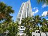 High-rise building featuring curved white balconies, floor-to-ceiling glass windows, and exterior palm landscaping