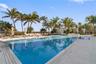 In-ground swimming pool featuring a tiled waterline, large stone-paver pool deck, integrated steps, and mature palm landscaping