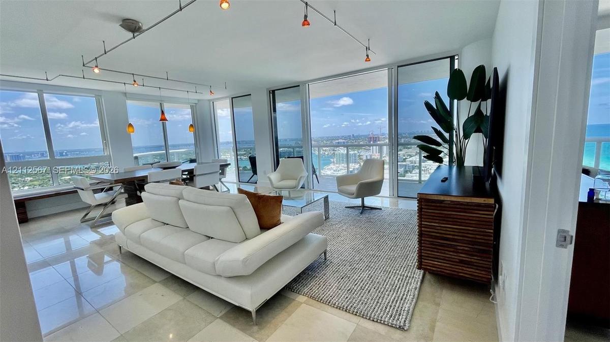 Living area featuring floor-to-ceiling glass walls, stone-finish tile flooring, and overhead track lighting