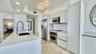 Kitchen featuring white flat-panel cabinetry, light-toned stone countertops, a waterfall-edge island, stainless steel appliances, and polished stone f