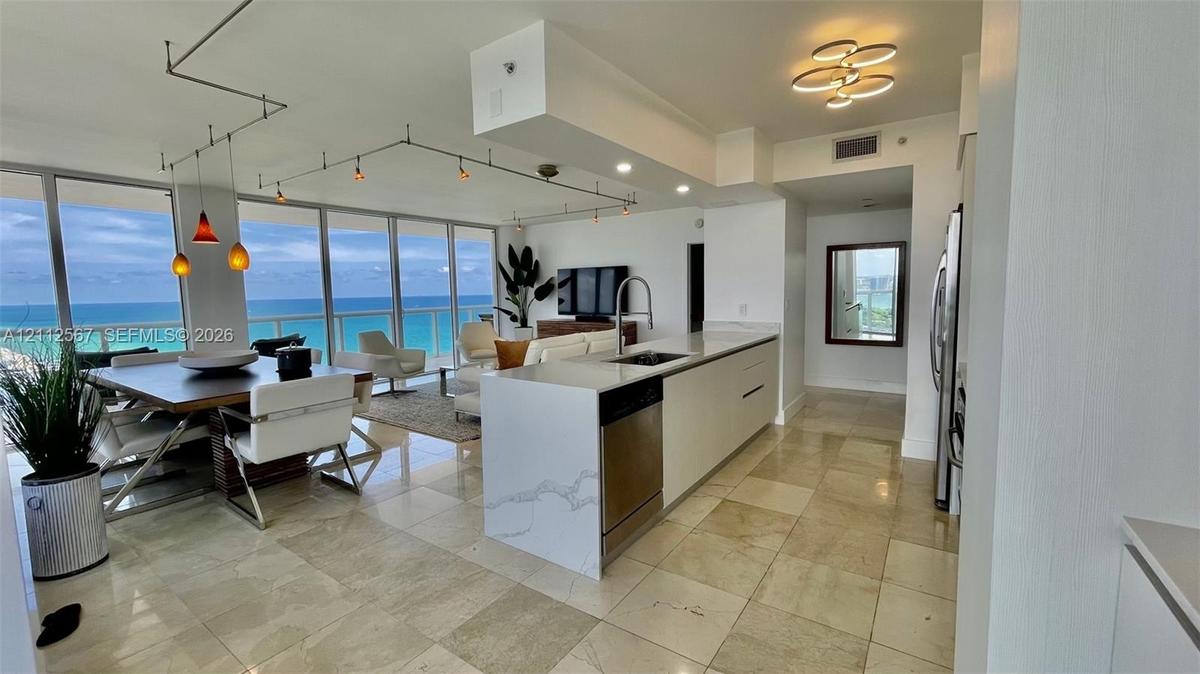 Open-concept kitchen featuring an island with a stone-finish countertop, stainless steel appliances, floor-to-ceiling windows, and natural stone floor
