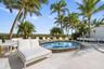 Circular in-ground spa featuring a stone-finish coping, surrounded by a paved deck, mature palm trees, and perimeter fencing