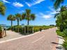 Brick-paver pathway surrounded by palm trees, coastal landscaping, and access to a sandy beach