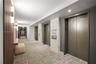 Common area featuring multi-panel elevator banks, vertical wood slat wall detailing, stone-clad pillar accents, recessed ceiling lighting, and wall-mo