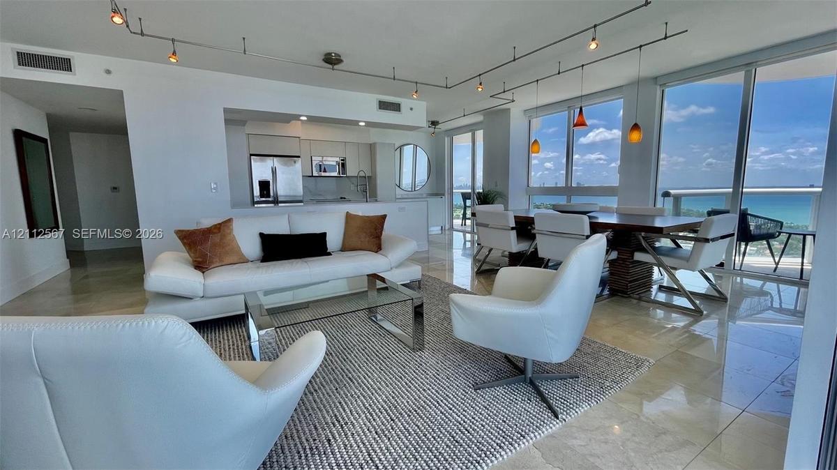 Open-concept living space featuring floor-to-ceiling windows, polished stone flooring, custom track lighting, and built-in kitchen cabinetry