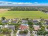 Aerial perspective featuring a property with a clay tile roof, paved circular driveway, private swimming pool, and expansive green space backdrop