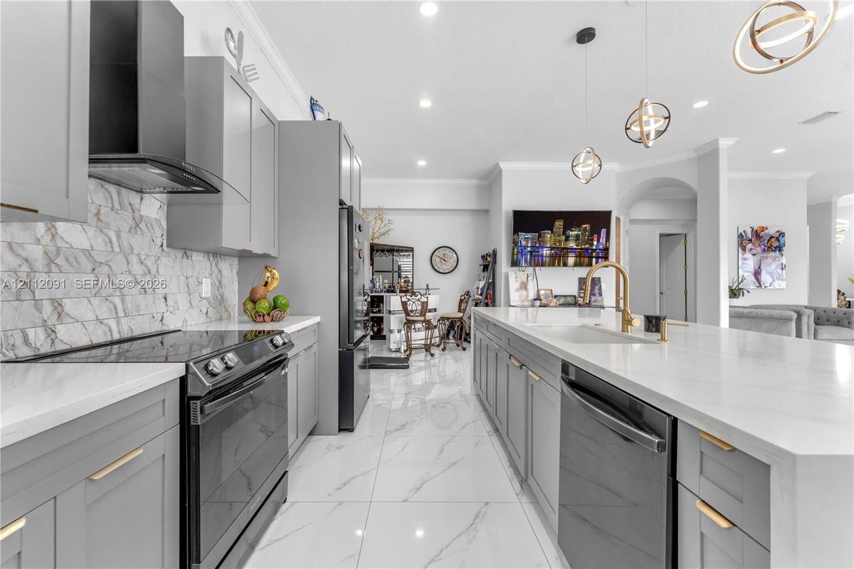 Kitchen featuring gray shaker-style cabinetry, a stone-pattern backsplash, quartz countertops, a central island with a gold-finish faucet, and large-f