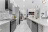 Kitchen featuring gray shaker-style cabinetry, a stone-pattern backsplash, quartz countertops, a central island with a gold-finish faucet, and large-f