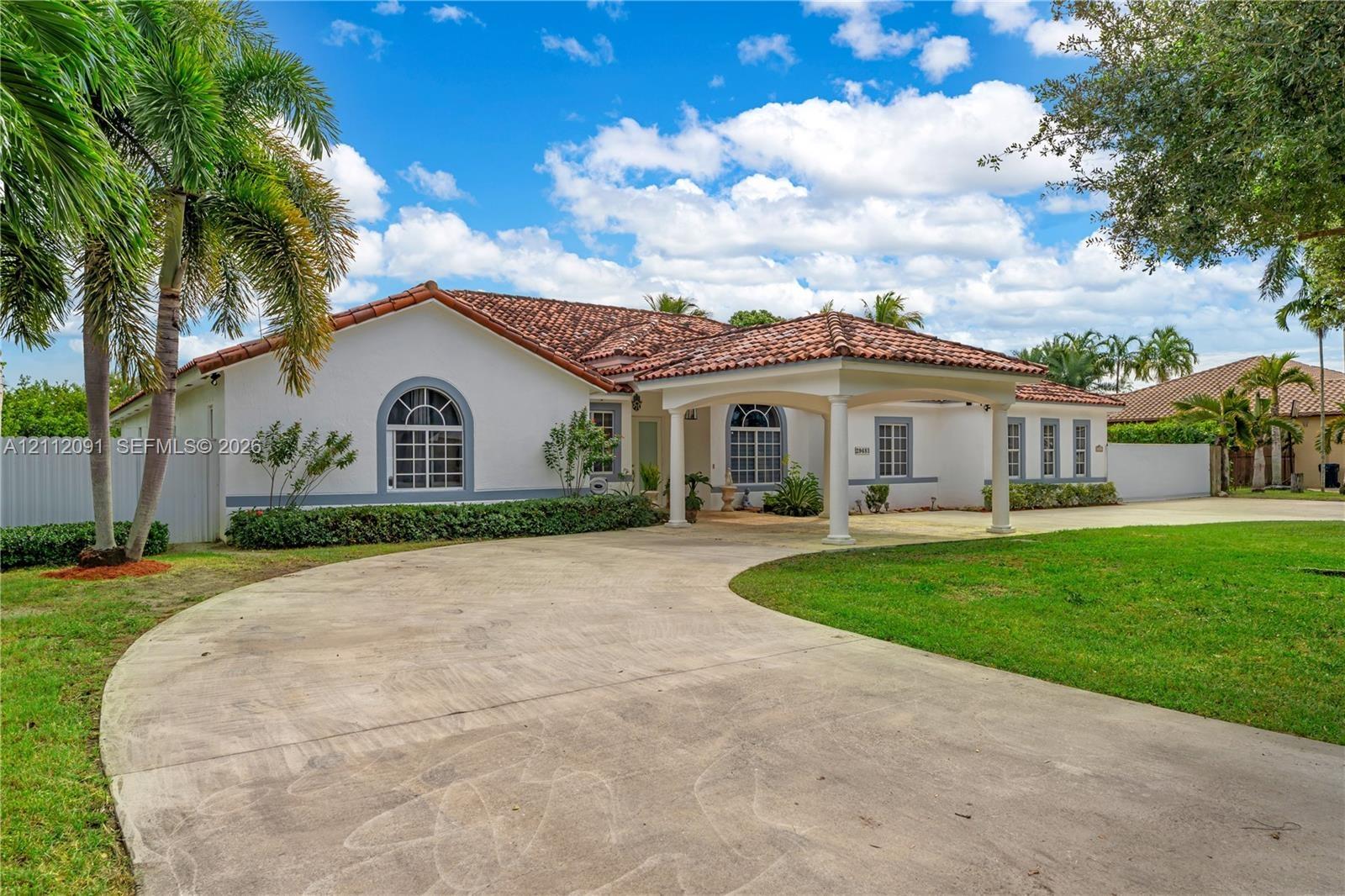 Single-story residence featuring a tile roof, arched windows, a covered porte-cochère, and a circular concrete driveway set on a landscaped lot