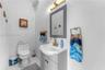 Grey vanity cabinet with a white basin, brass-finish faucet, framed wall mirror, modern linear wall-mounted lighting, and tile flooring