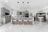 Kitchen featuring light-gray shaker-style cabinetry, quartz countertops, a stone-tile backsplash, polished large-format tile flooring, and three conte