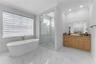 Freestanding soaking tub with gold-tone fixtures, walk-in glass-enclosed shower with tiled surround, stone-finish vanity countertop, and polished tile