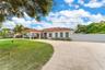 Single-story residence featuring a clay tile roof, covered porte-cochère, multi-pane windows, expansive concrete motor court, and perimeter privacy fe