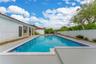 In-ground swimming pool with tile border, expansive concrete decking, covered patio with structural columns, and perimeter privacy fencing