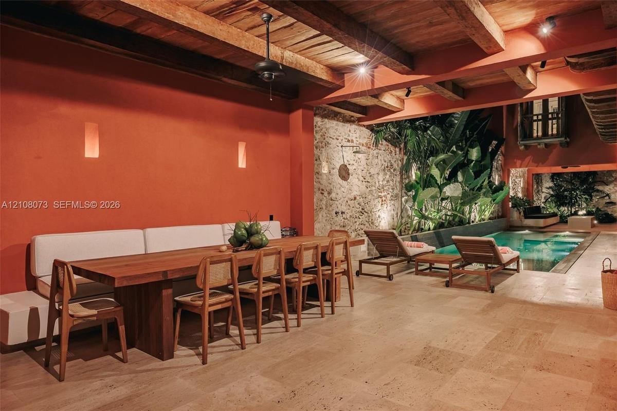 Covered patio featuring exposed wood-beam ceilings, stone masonry wall accents, neutral-toned tile flooring, and an integrated swimming pool