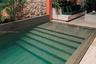 In-ground pool featuring integrated steps, natural stone wall, masonry tiered planter, and stone tile decking