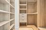Custom walk-in closet featuring wood-finish cabinetry, built-in shelving, integrated drawers with metal pulls, and polished metal hanging rods