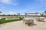 Outdoor terrace featuring light-toned stone paving, a swimming pool, a wood-frame pergola, synthetic turf, and an oversized permanent outdoor chess bo