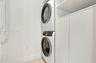 Laundry area featuring a stackable front-load washer and dryer, integrated white cabinetry with open shelving, and light-toned flooring